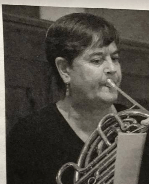 Fleur Barnes-Rowell, sitting, playing horn