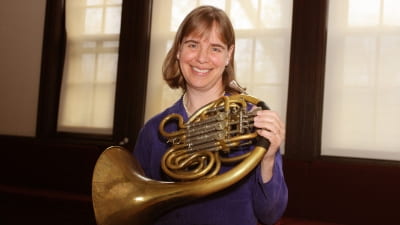 Jean Jeffries standing with french horn, indoors, smiling